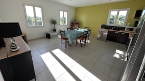 Une cuisine lumineuse avec un coin repas, comprenant une table avec des chaises, une plante en pot et une lampe moderne.