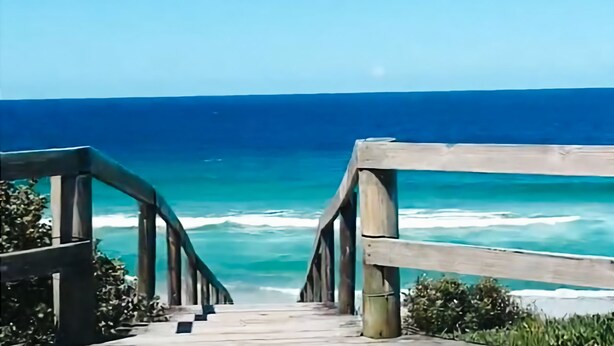 Unes escales de fusta que porten a una platja amb vistes a l'oceà.