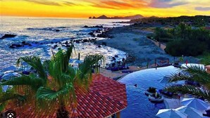 Un complexe hôtelier de bord de mer offrant une vue sur l’océan, des palmiers et un coucher de soleil.