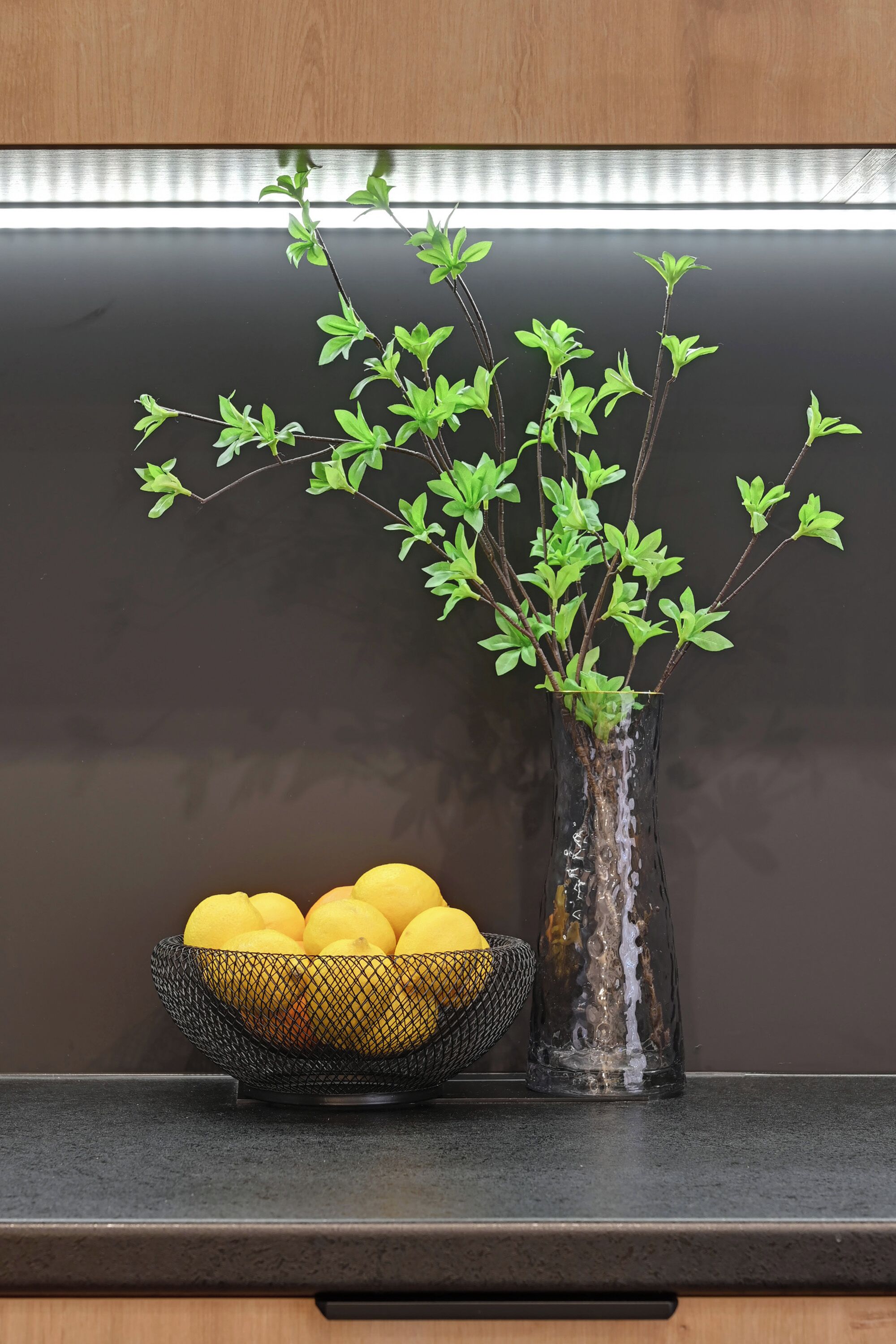 Una encimera de cocina con un florero con ramas verdes y un cuenco de limones.