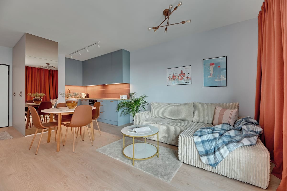 Ein modernes Wohnzimmer mit einer Couch, einem Esstisch mit Stühlen, einem kleinen Couchtisch und einer Küche im Hintergrund.