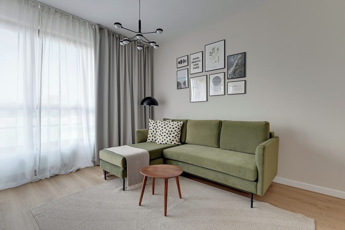 Ein modernes Wohnzimmer mit einem grünen Sofa, einem kleinen Holztisch und einem weißen Teppich.