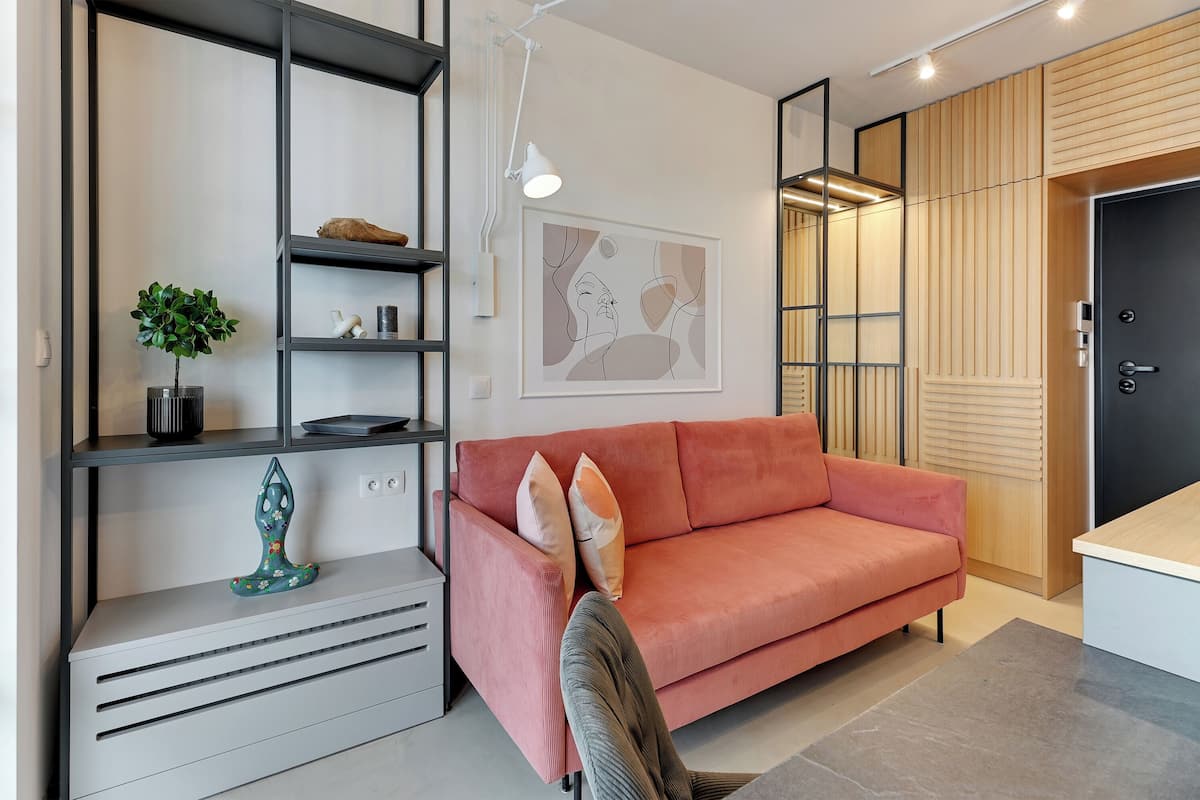 Ein modernes Wohnzimmer mit einem roten Sofa, einem grauen Konsolentisch, einer grünen Pflanze und einem gerahmten abstrakten Kunstwerk an der Wand.