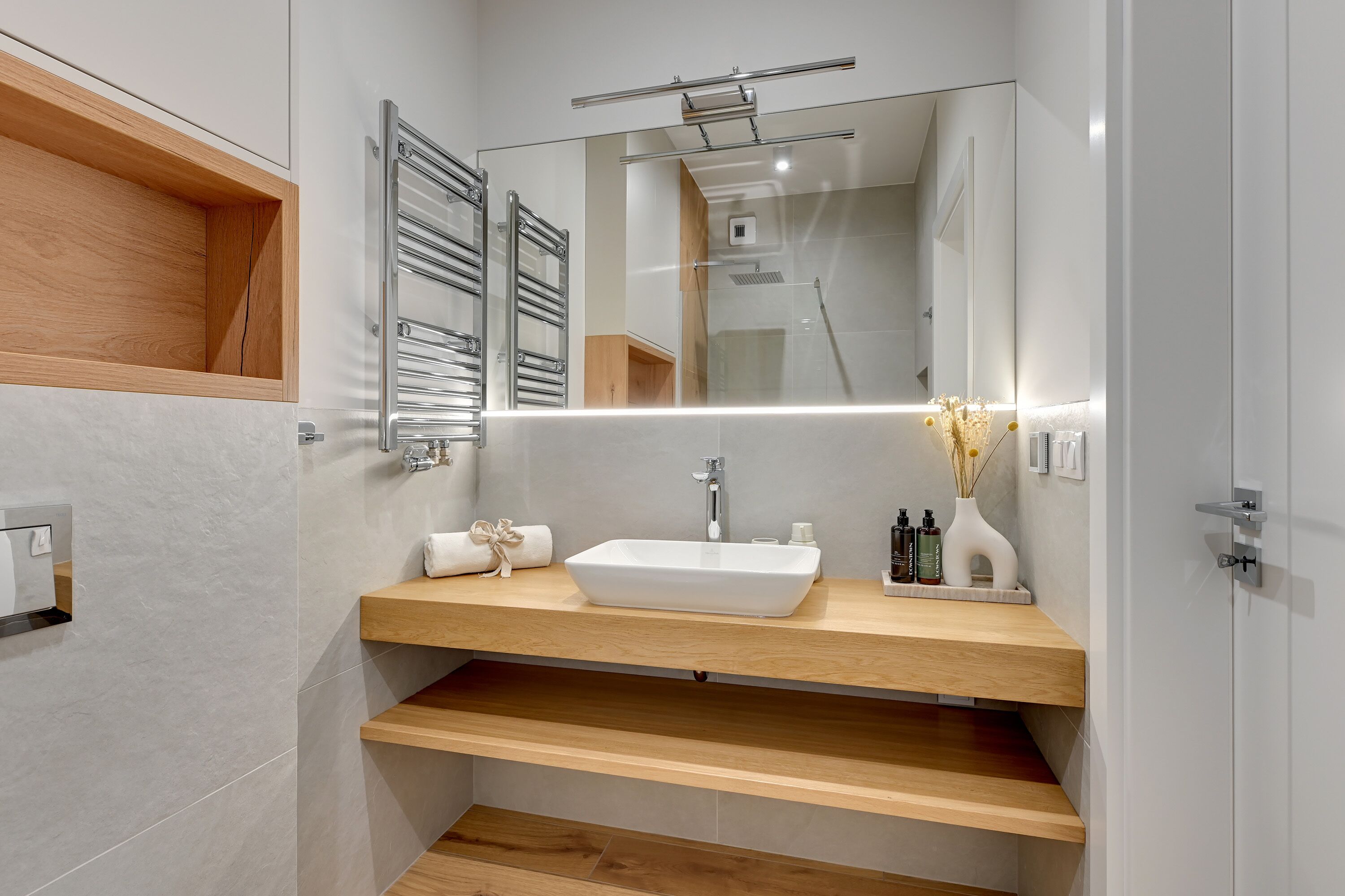 A modern bathroom with a wooden vanity, a large mirror, and a built-in shower.
