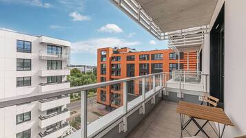 Un balcón con mesa y sillas de madera, con vistas a un edificio moderno de fachadas anaranjadas y blancas.
