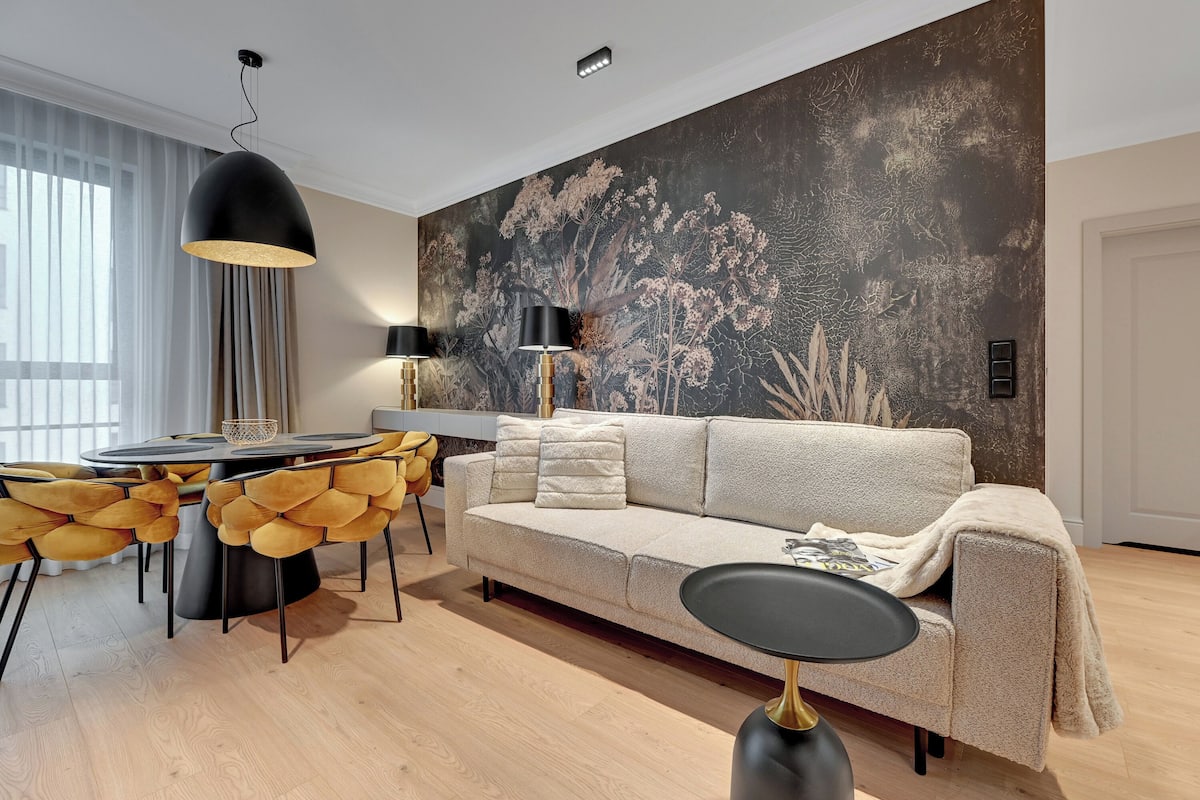 Ein modernes Wohnzimmer mit einem beigefarbenen Sofa, gelben Polsterstühlen, einem runden Esstisch und einem großen, abstrakten Wandbild.