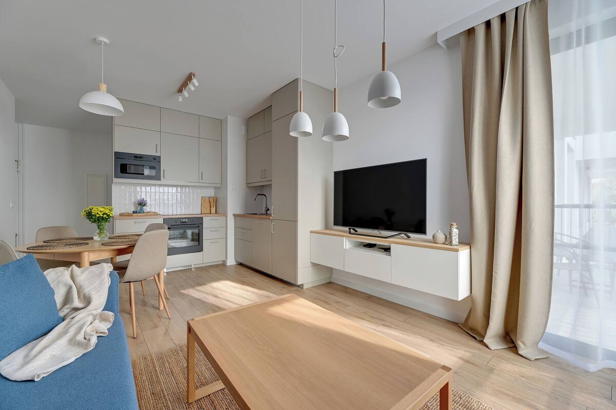 Ein modernes Wohnzimmer mit Sofa, Fernseher, Esstisch und Küchenbereich.