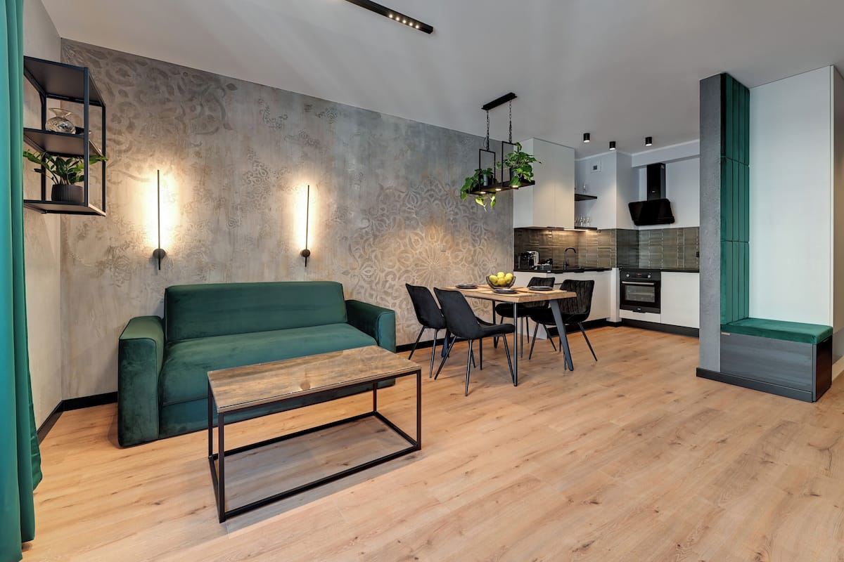 Ein moderner Wohnraum mit einem grünen Sofa, einem Holztisch und einem Essbereich inklusive Tisch und Stühlen.