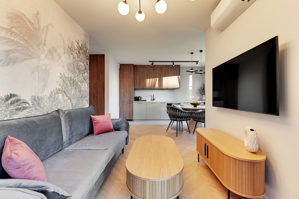 Ein modernes Wohnzimmer mit grauem Sofa, Holztisch und Wandfernseher.