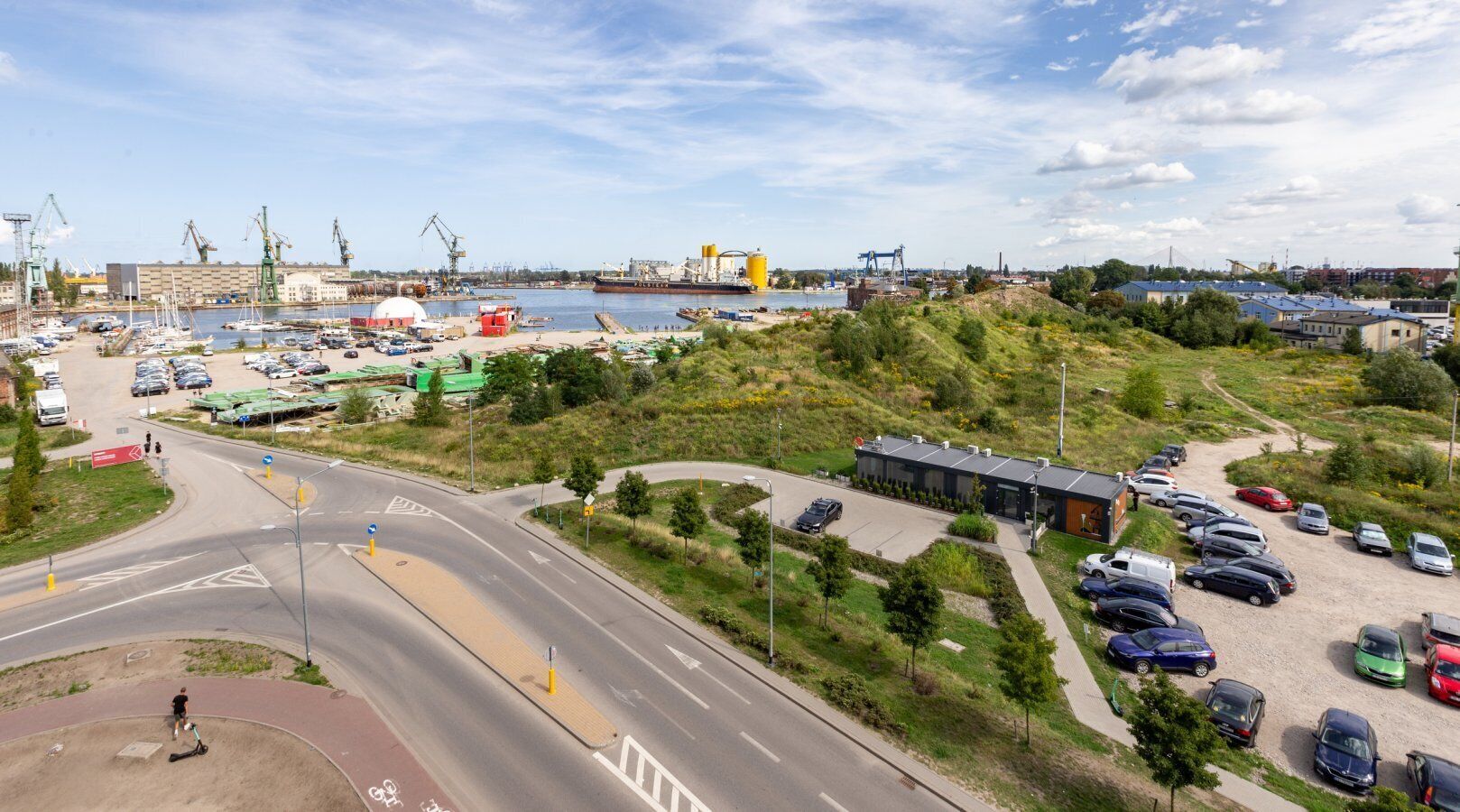 An aerial view of a coastal area with a marina, parked cars, and industrial buildings.