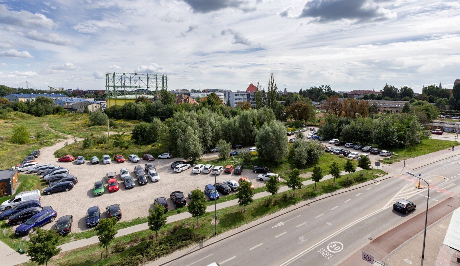 A parking lot with various cars, a road with a speed limit sign, and a bridge in the background.