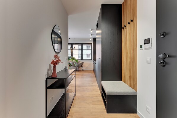 A modern hallway with a wooden bench, a black-framed mirror, and a small table with a vase. - Doki Living - Foodhall & Parking by Downtown Apartments (Gdansk)