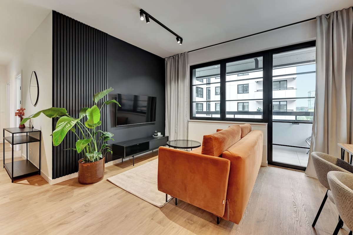 Ein modernes Wohnzimmer mit Sofa, Fernseher und großen Fenstern.