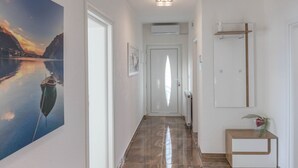 A hallway with a painting of a boat on water, a door with a frosted glass panel, a radiator, and a small wooden side table with a plant. - Spacious Novi Vinodolski Apartments With Terrace and Shared Pool (Crikvenica)