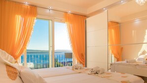 A hotel room with a bed, a bathroom, and a balcony with orange curtains. - Spacious Novi Vinodolski Apartments With Terrace and Shared Pool (Crikvenica)