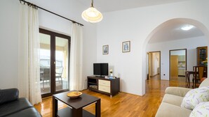 A living room with a sofa, a coffee table, a TV stand, and a dining area with chairs. - Graceful Apartment With Barbecue Area (Porec)