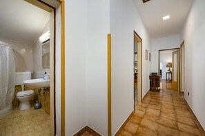 A hallway leading to a bathroom with a toilet, sink, and shower.