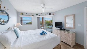 A hotel room with a bed, a television, a dresser, and a balcony with a view of the sea.