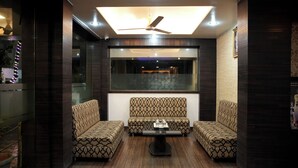 A modern living room with a ceiling fan, a large window, and patterned sofas. - Hotel Mathura Inn (Rahata)