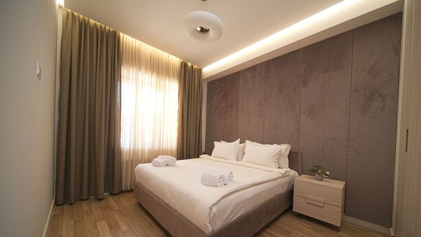 Ein modernes Hotelzimmer mit einem großen Bett, Holzboden, einem Nachttisch und einer Wandanlage.