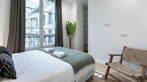 Ein Hotelzimmer mit einem Bett, einem Sessel, einer Pflanze und Blick auf Gebäude durch das Fenster.