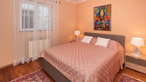 A bedroom with a bed, two bedside tables, a nightstand, a window with lace curtains, and a painting on the wall. - Graceful Apartment in Nature (Porec)