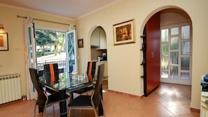 A dining area with a glass table and chairs, a view through a glass door, and a red door leading to another room. - Graceful Apartment in Nature (Porec)