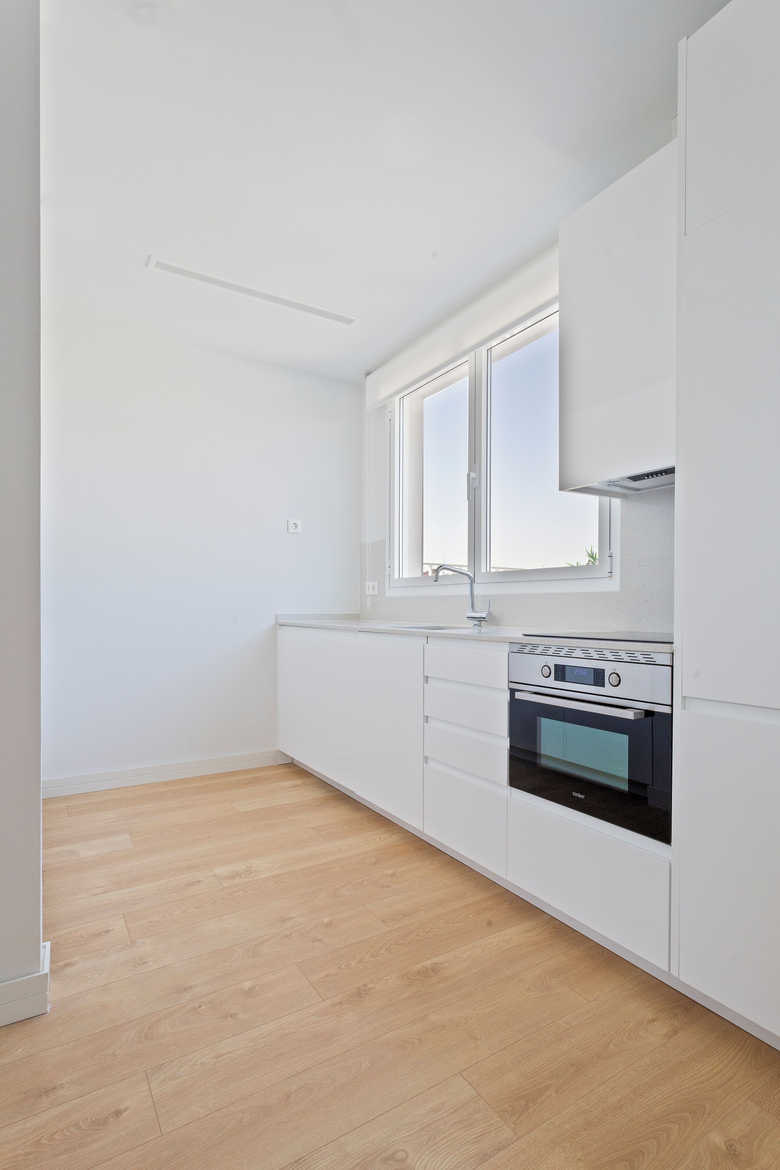 Una cocina moderna con armarios blancos, horno empotrado y ventana sobre el fregadero.