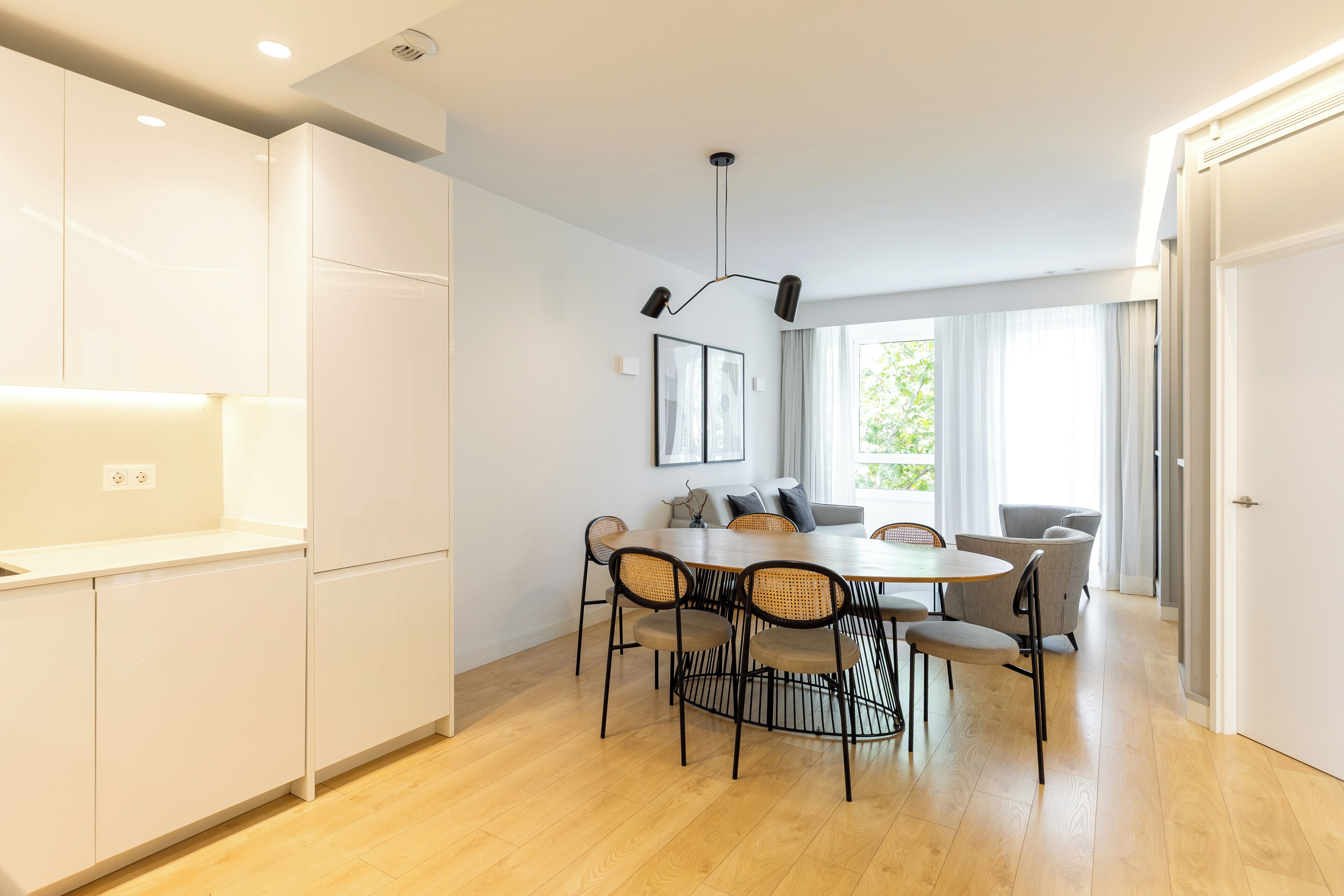 A modern kitchen with white cabinets, a dining table with chairs, and a pendant light.