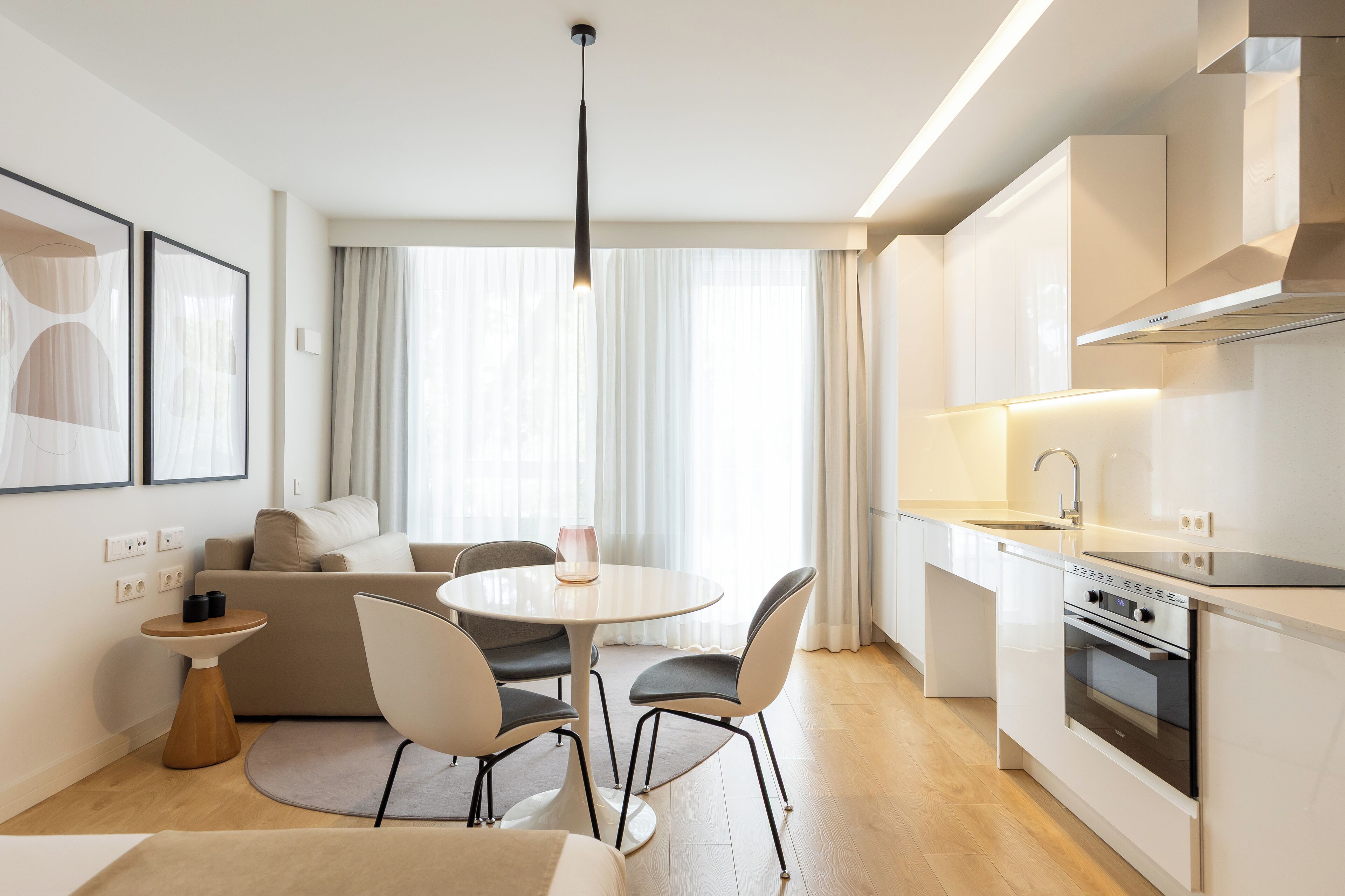 A modern kitchen with a built-in oven, a dining area with a round table and chairs, and a living area with a sofa and a coffee table.