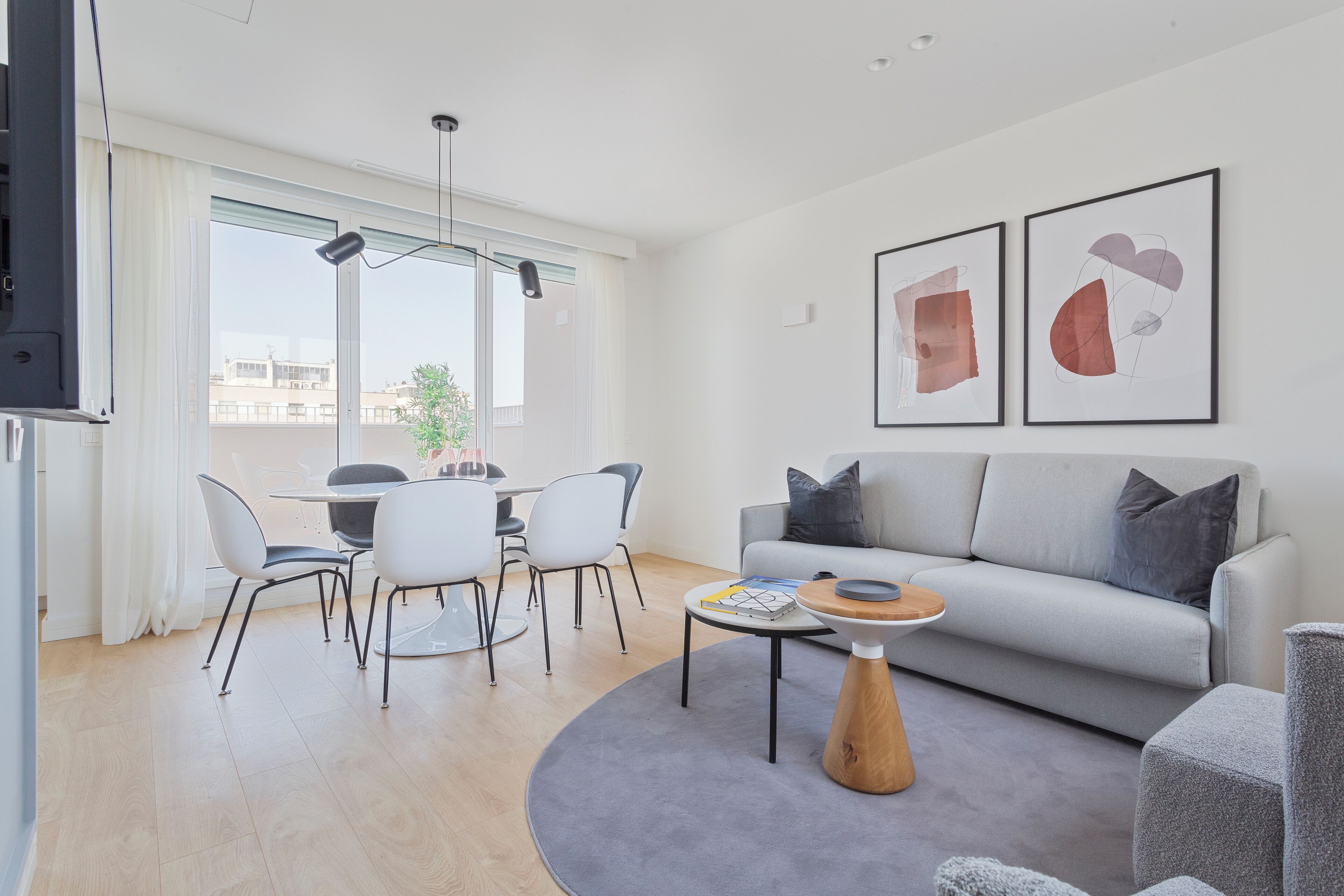 A modern living room with a grey sofa, a coffee table, and a dining area with chairs and a table.