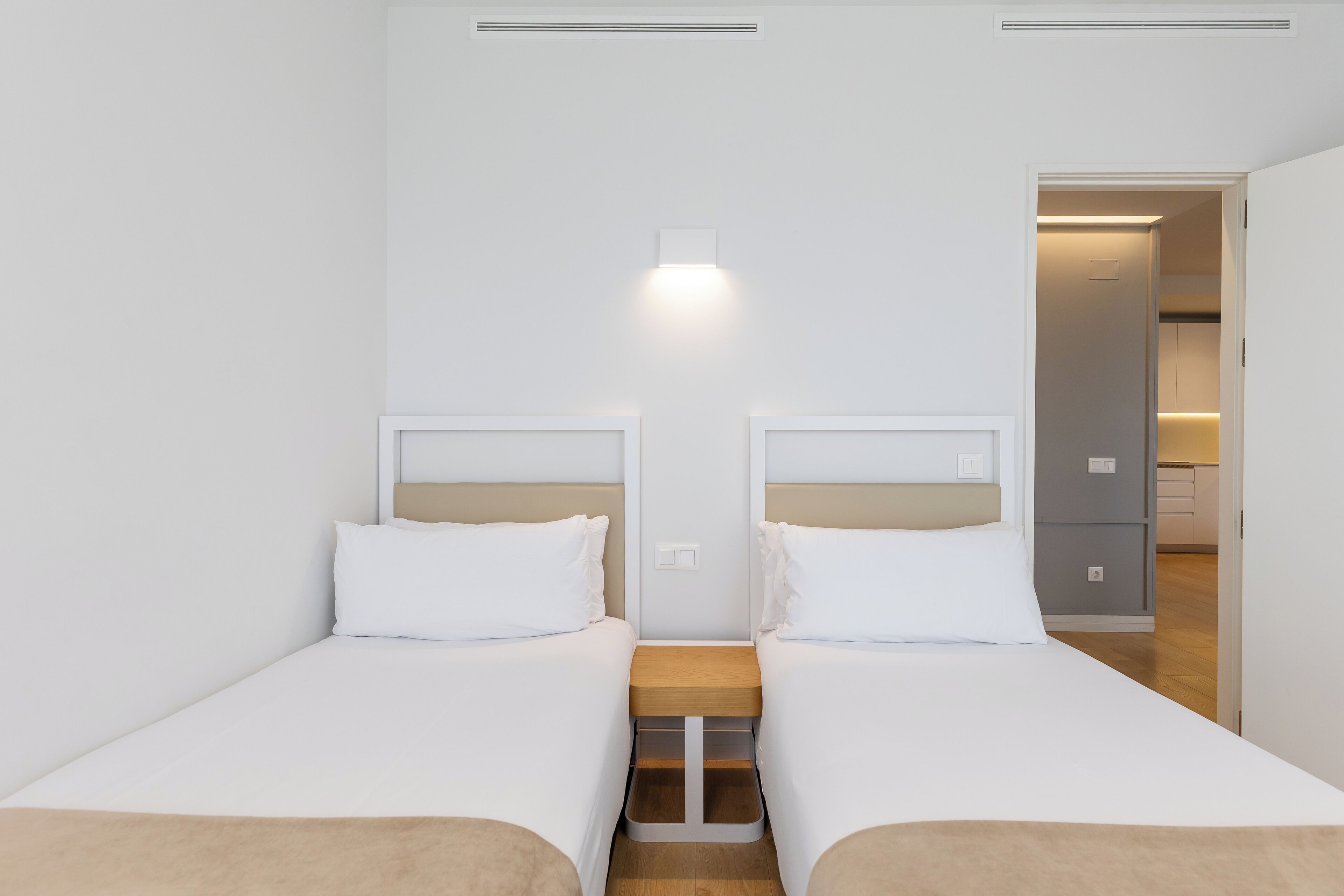 Habitación de hotel con dos camas individuales, una mesita de noche de madera y una lámpara sobre la mesita.