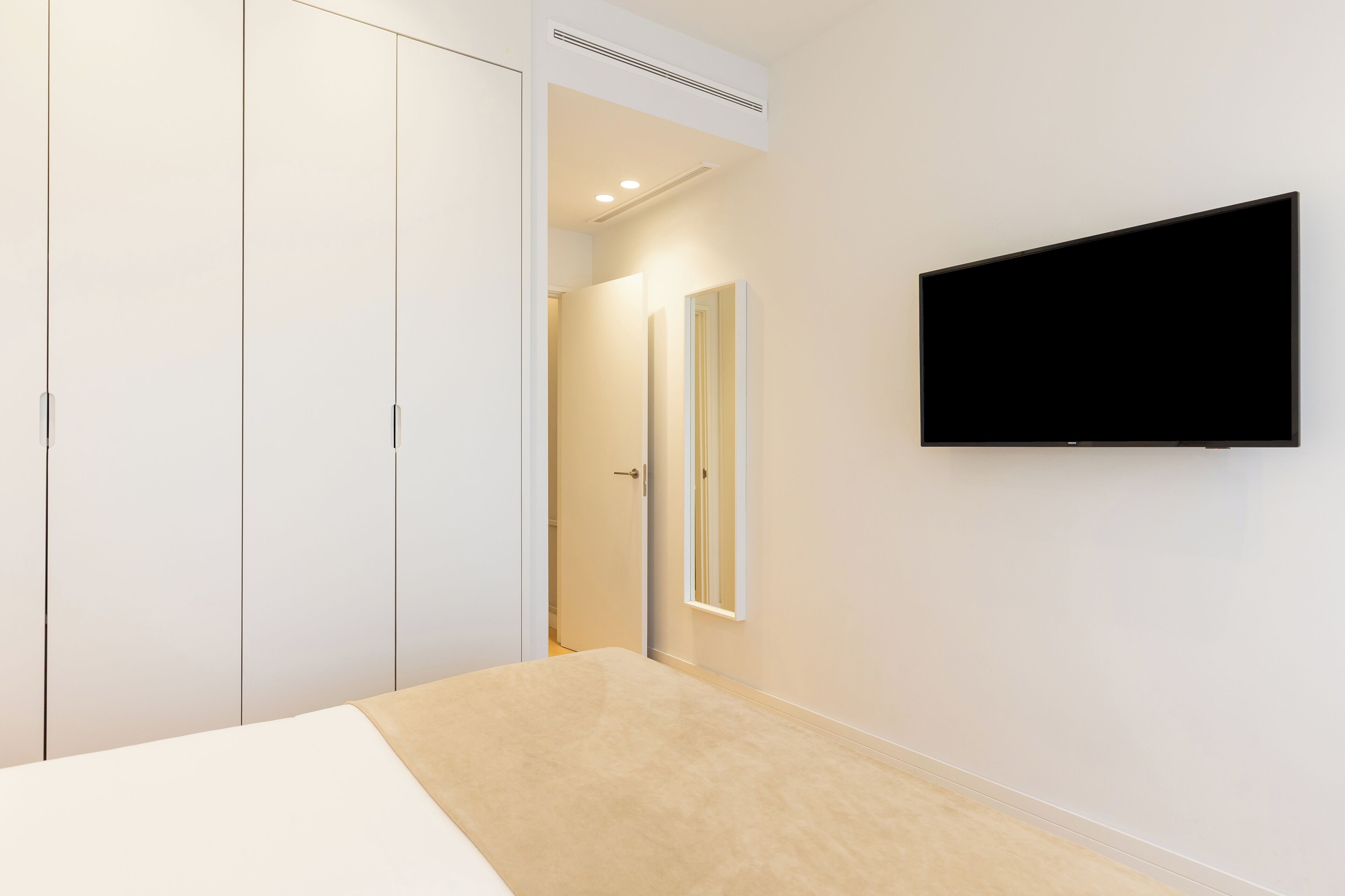 A bedroom with a bed, a TV mounted on the wall, and a wardrobe.