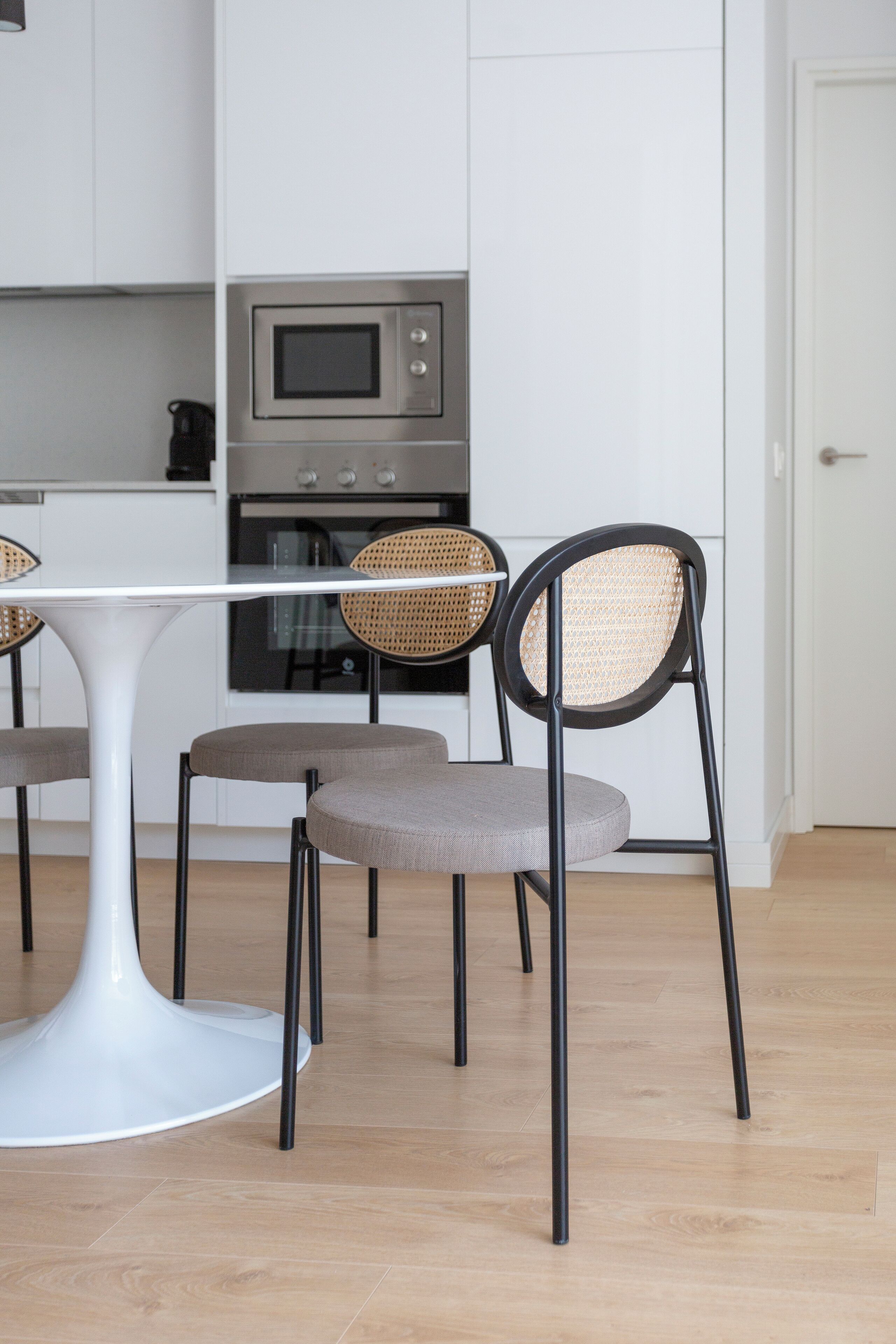 A modern kitchen with white cabinetry, a white dining table, and two chairs with woven seats.