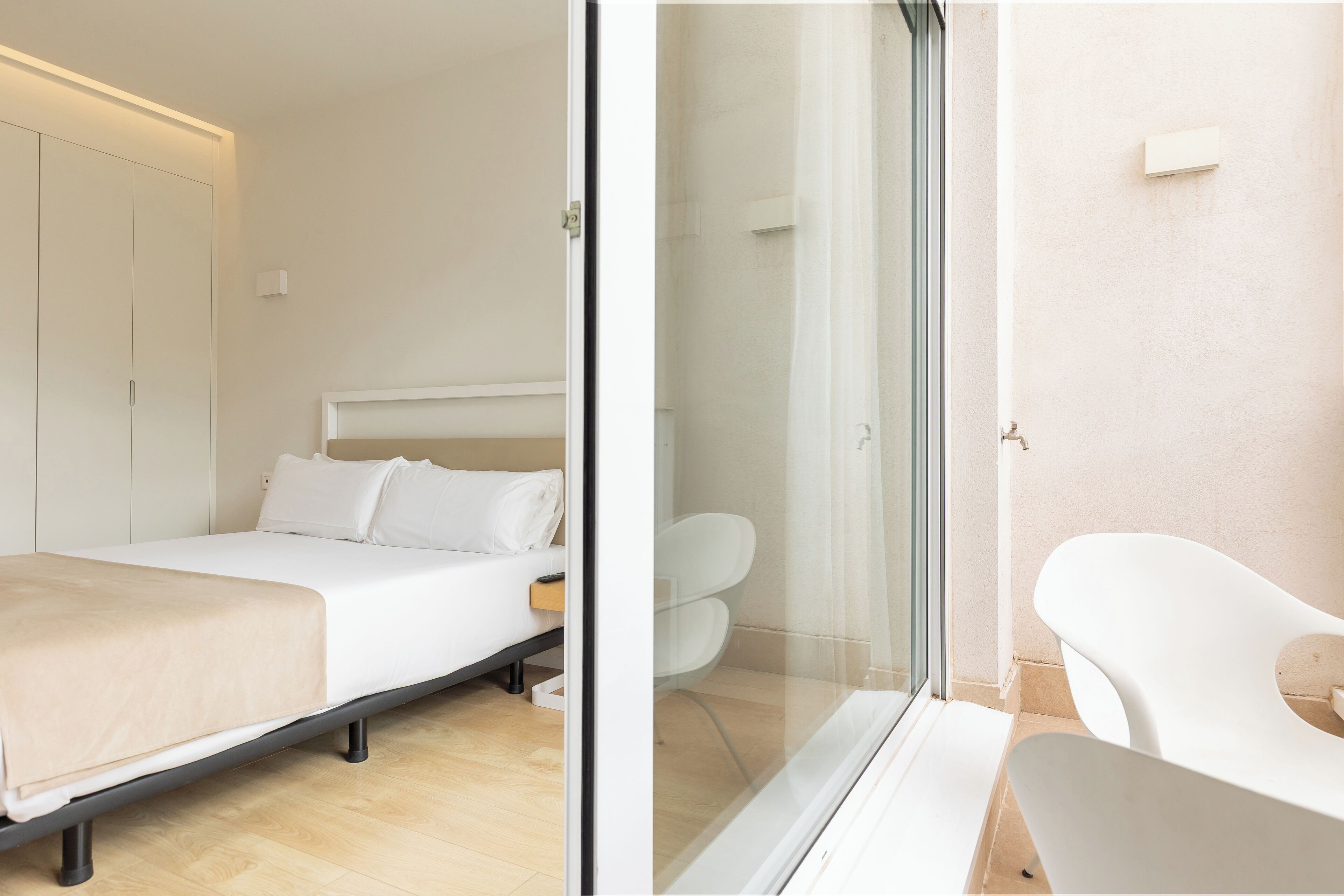 Une chambre moderne avec un lit, une table de chevet et une porte en verre donnant sur une salle de bain équipée d’une douche et de toilettes.