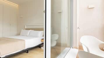 Un dormitorio moderno con cama, mesita de noche y una puerta de vidrio que da a un baño con ducha e inodoro.