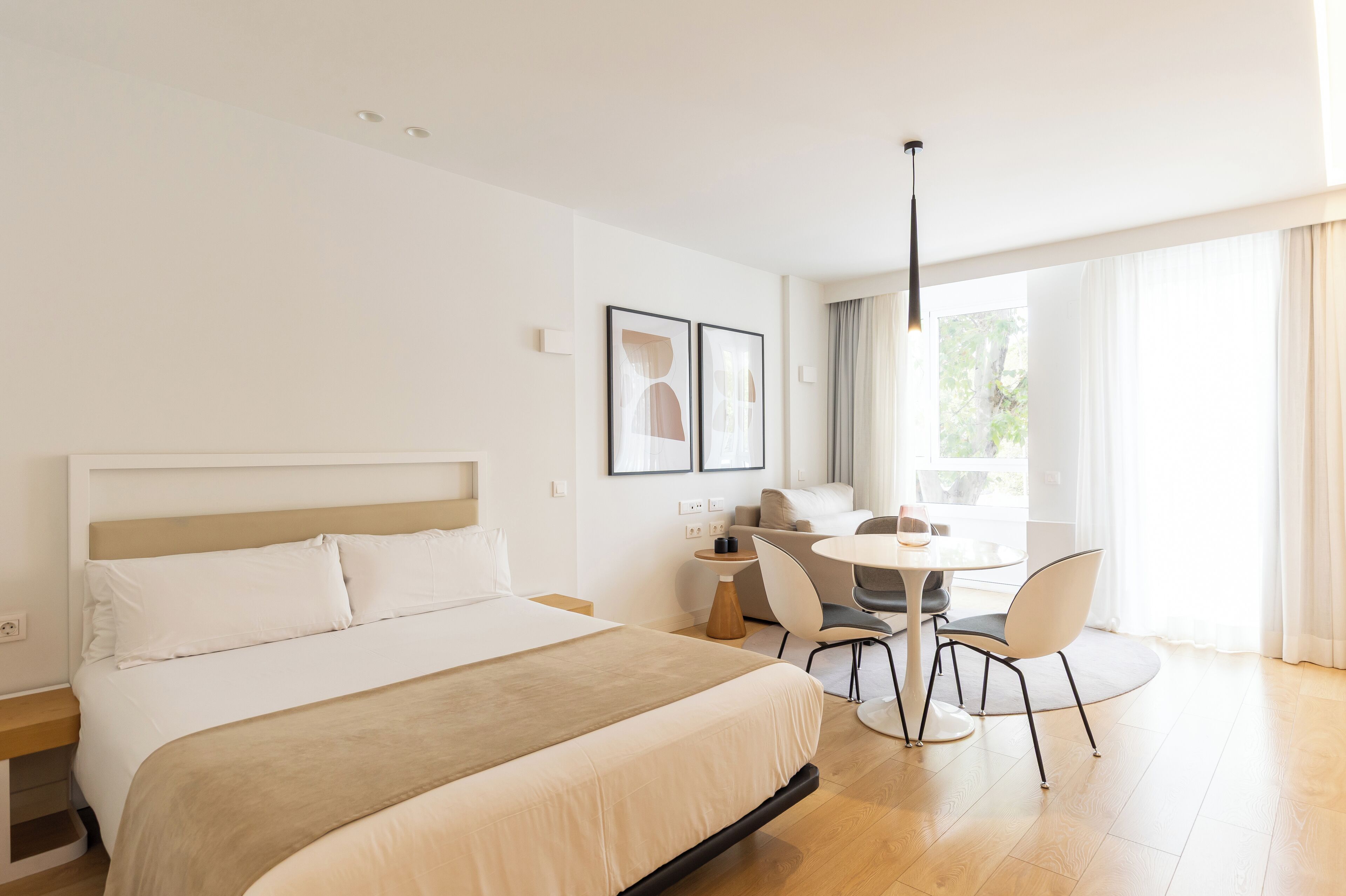 Une chambre d’hôtel moderne dotée d’un grand lit, d’un coin repas avec une table et des chaises, et d’une grande fenêtre avec des rideaux.