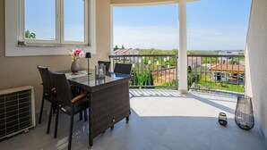 Ein Balkon mit Tisch und Stühlen, eine Vase mit Blumen und Blick auf die umliegende Landschaft.