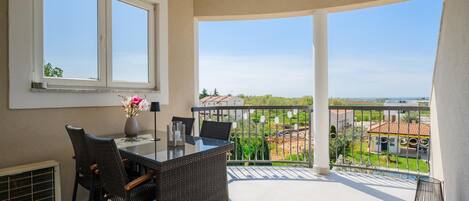 Uma varanda com mesa e cadeiras, um vaso com flores e vista para a paisagem ao redor.