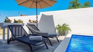 Ein Poolbereich mit zwei Liegestühlen, einem großen Sonnenschirm und einem Blumentopf.