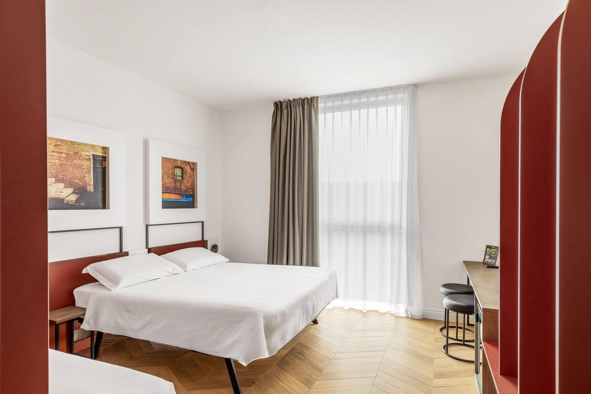 Een hotelkamer met een bed, een bureau, twee stoelen en kunstwerken aan de muur.