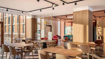 A modern interior with round tables and chairs, a large wooden column, and a view through large windows.