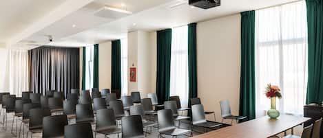 Un salón de conferencias con filas de sillas, una larga mesa y un proyector.