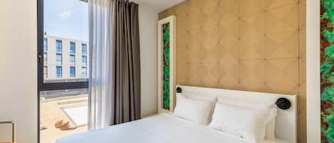 A hotel room with a bed, a view of the outside, a door, and a wall with a geometric pattern.