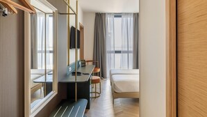 Une chambre d’hôtel comprenant un lit, un bureau avec une chaise, un miroir et une armoire.