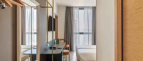 Una habitación de hotel con cama, escritorio, silla, espejo y armario.