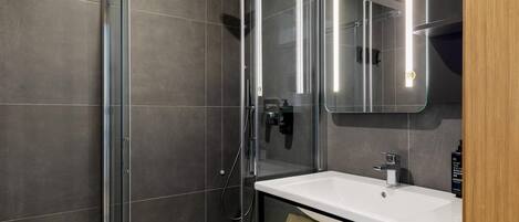 A modern bathroom with a glass-enclosed shower, a white sink, and a mirror above it.