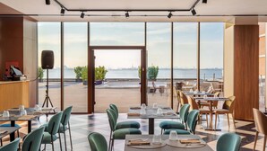 Un restaurant avec des tables et des chaises, de grandes fenêtres et une vue sur l’eau.