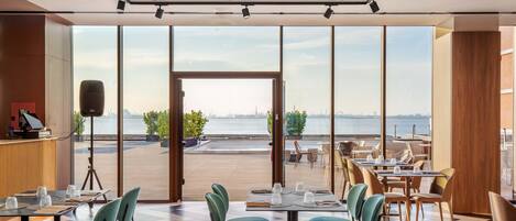A restaurant with tables and chairs, large windows, and a view of the water.