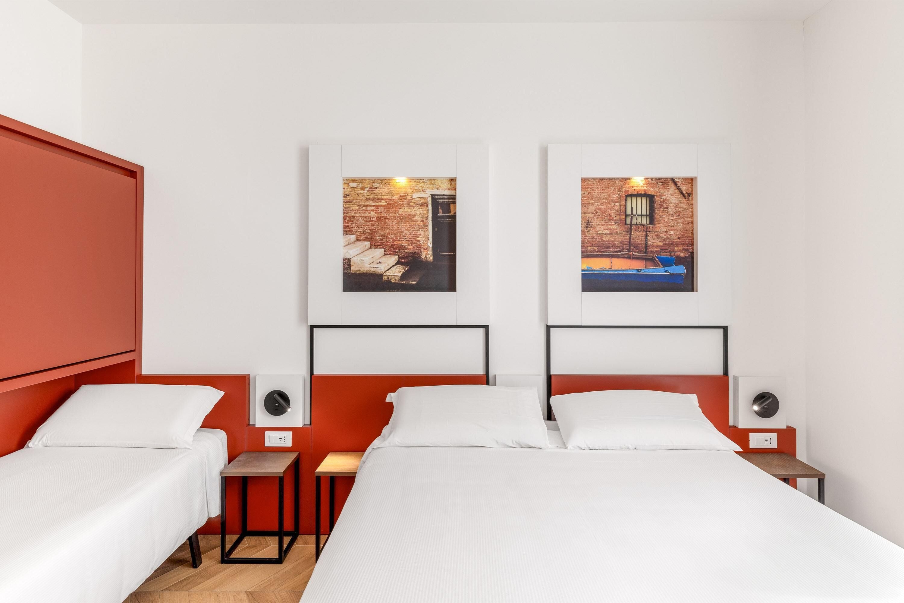 Une chambre d’hôtel avec deux lits, un mur d’accent de couleur rouge et deux tableaux encadrés accrochés au mur.